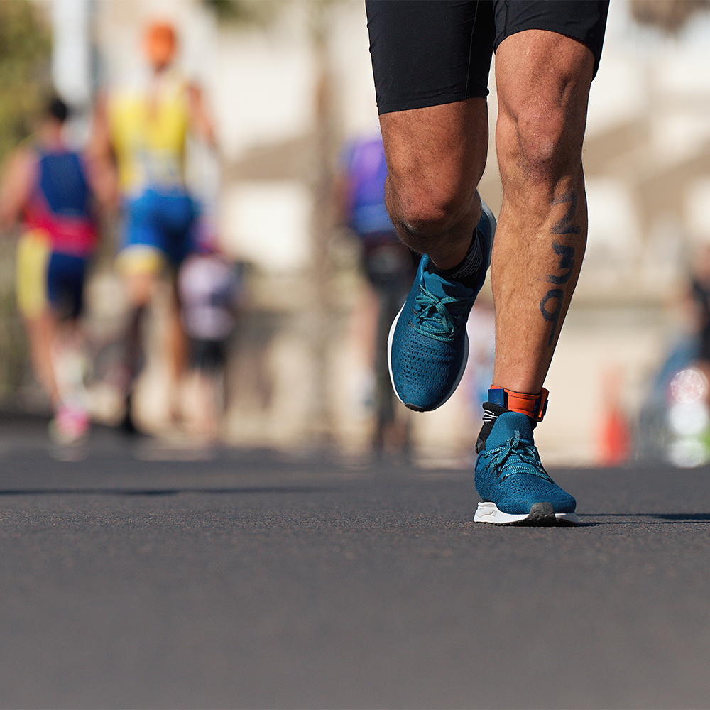Close-up of a runner's legs on a sunlit road during a marathon event.